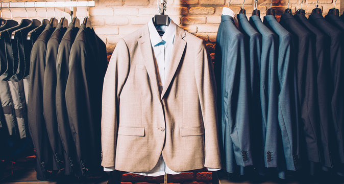 Men formal wear. Classy outfit. Modern clothing store. Business suit jackets and vests hanging, displayed over brick wall.