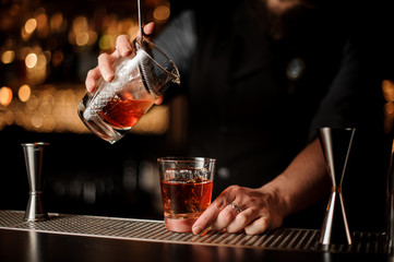 Male bartender pours alcohol cocktail with strainer