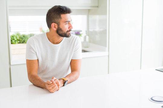 Handsome hispanic man casual white t-shirt at home looking to side, relax profile pose with natural face with confident smile.