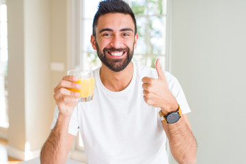 Fototapeta premium Handsome hispanic man drinking healthy orange juice happy with big smile doing ok sign, thumb up with fingers, excellent sign