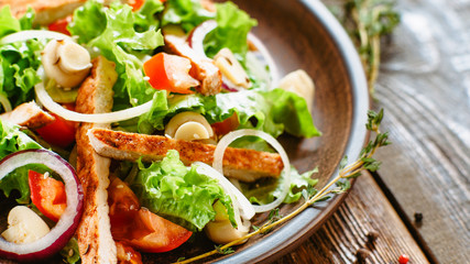 Restaurant kitchen menu. Cropped closeup of chicken salad with vegetables. Served in rustic clay plate on wooden table.
