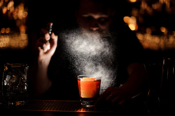 Darkened close shot of bartender pouring cocktail using sprayer