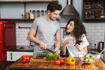 Picture of happy couple cooking salat with vegetables together in modern kitchen at home