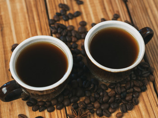 Two small cups of freshly brewed espresso on a wooden background with scattered coffee beans