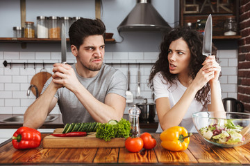 Picture of amusing funny couple cooking salat with vegetables together in modern kitchen at home