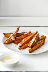 Homemade caramelized roasted sliced yams or sweet potato with Greek-style yogurt and crushed red-pepper flakes on white wooden background with copy space for text.Healthy vegetable yummy side-dish