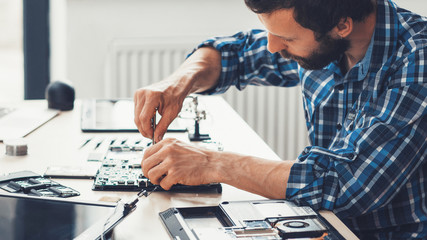 Computer repair service. Electronic hardware support. Side view of bearded technician fixing damaged laptop.