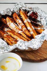 Homemade caramelized roasted in foil sliced yams or sweet potato with Greek-style yogurt and crushed red-pepper flakes close-up on white wooden background.Healthy vegetable yummy side-dish