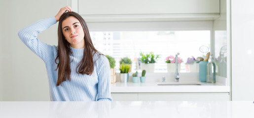 Fototapeta na wymiar Wide angle picture of beautiful young woman sitting on white table at home confuse and wonder about question. Uncertain with doubt, thinking with hand on head. Pensive concept.