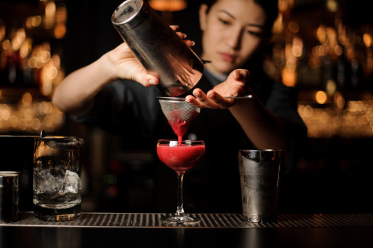 Female bartender pouring a cocktail with the shaker and sieve