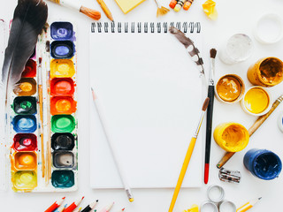 Creative artist workplace. Art workshop. Painting hobby. Flat lay of blank mockup sketchbook, pencils, paintbrushes and palettes.