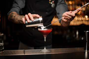 Fototapeta na wymiar Bartender pouring cocktail using shaker and spoon