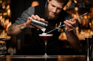 Male bartender makes cocktail using shaker and spoon