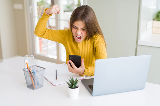 Beautiful Young Girl Kid Using Smartphone And Computer Laptop Annoyed And Frustrated Shouting With Anger, Crazy And Yelling With Raised Hand, Anger Concept