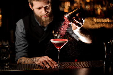 Bartender sprinkles an alcohol cocktail in glass