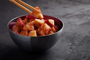Kimchi Radish in a spicy pickling sauce Kkakdugi close-up.Korean traditional crunchy spicy fermented vegetables in bowl on dark grey background with copy space.Probiotic and fermented foods concept