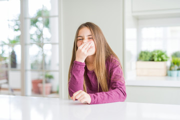 Beautiful young girl kid on white table smelling something stinky and disgusting, intolerable...