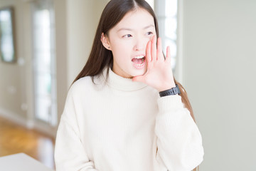 Beautiful Asian woman wearing casual sweater shouting and screaming loud to side with hand on mouth. Communication concept.