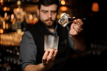 Portrait of bartender holding glass and ice with tongs