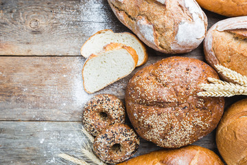 Assortment of fresh baked bread and buns on wooden table background, top view