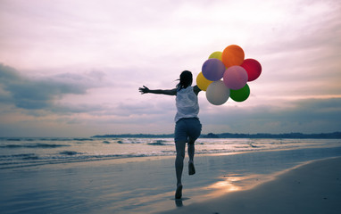 young asian woman running and jumping on seaside with colored balloons