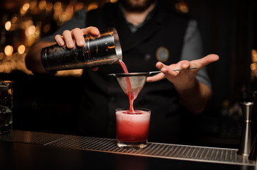 Fototapeta na wymiar Bartender pours alcohol drink using shaker and sieve
