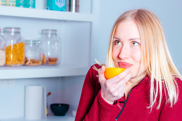 Portrait of beautiful young woman in the kitchen smelling an orange freshly cut in half. Healthy food concept.