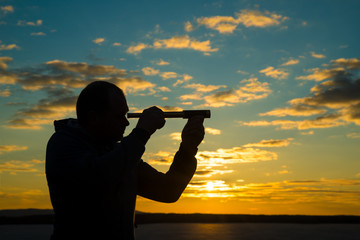 A man looks into a use monocular telescope against a dramatic sky at sunset. business concept idea, look to the future, look, spy. Businessman. Vision