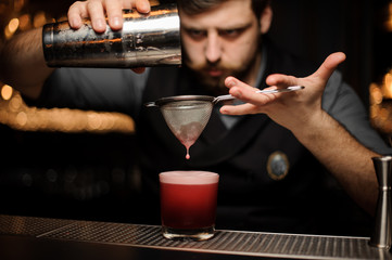 Bartender makes an alcohol drink using shaker and sieve
