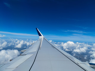 Fototapeta na wymiar Wing of an airplane above the clouds with a bright blue sky on a sunny day.