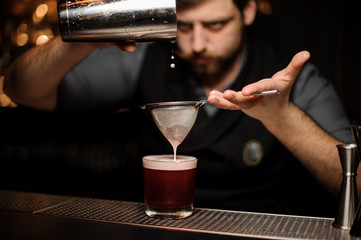 Fototapeta na wymiar Bartender prepares alcohol drink with a shaker and sieve