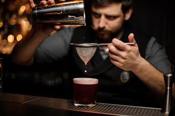 Bartender preparing alcohol drink with the shaker and sieve