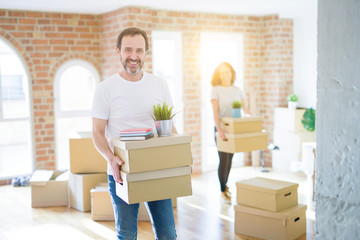 Middle age senior couple moving to a new house, man smiling happy in love with new apartment and holding cardboard boxes
