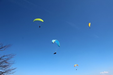 Athletes paragliding over mountains infront of blue cloudless sky