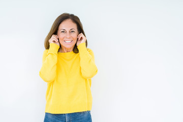 Beautiful middle age woman wearing yellow sweater over isolated background covering ears with fingers with annoyed expression for the noise of loud music. Deaf concept.