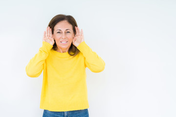 Fototapeta premium Beautiful middle age woman wearing yellow sweater over isolated background Trying to hear both hands on ear gesture, curious for gossip. Hearing problem, deaf