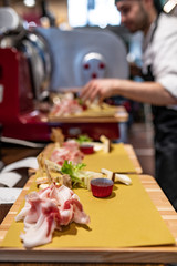 Uomo all macchina affettatrice che prepara antipasti di affettati su taglieri in legno