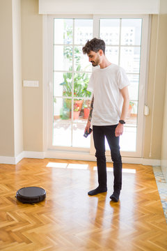 Young man using automatic vacuum cleaner to clean the floor, controling machine housework robot