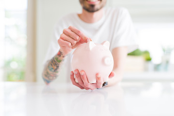 Close up of man putting a coin inside piggy bank as savings smiling