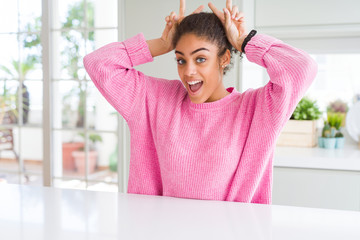 Fototapeta na wymiar Beautiful african american woman with afro hair wearing casual pink sweater Posing funny and crazy with fingers on head as bunny ears, smiling cheerful
