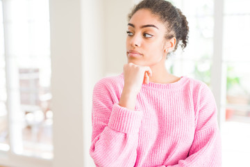 Beautiful young african american woman with afro hair with hand on chin thinking about question, pensive expression. Smiling with thoughtful face. Doubt concept.