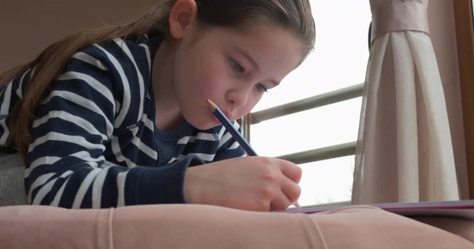 A pre-school girl drawing with pencils at home