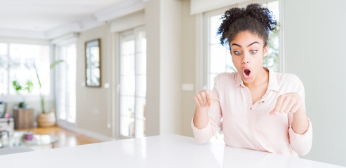 Wide angle of beautiful african american woman with afro hair Pointing down with fingers showing advertisement, surprised face and open mouth