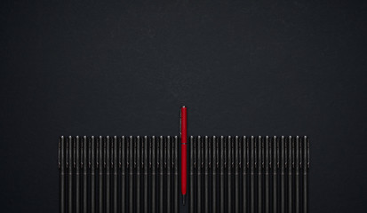 Red pen standing out from the row of black pen . Flat lay and top view with copy space on black background .