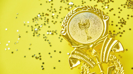Fototapeta na wymiar Champion gold cup trophy on yellow background. minimalism style, victory celebration concept. and golden stars of confetti are scattered around