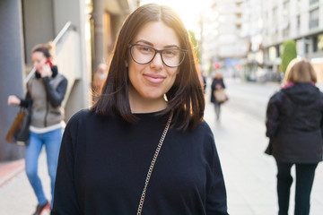 Beautiful young brunette woman smiling excited walking down the city streets, happy and confident expression standing outdoors at the town