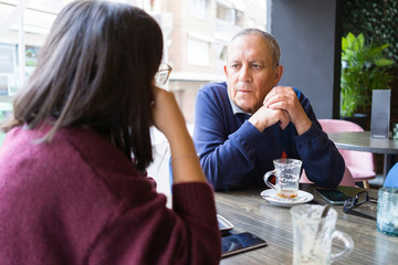 Senior man having a conversation with woman drinking coffee and relaxing, chatting at restaurant