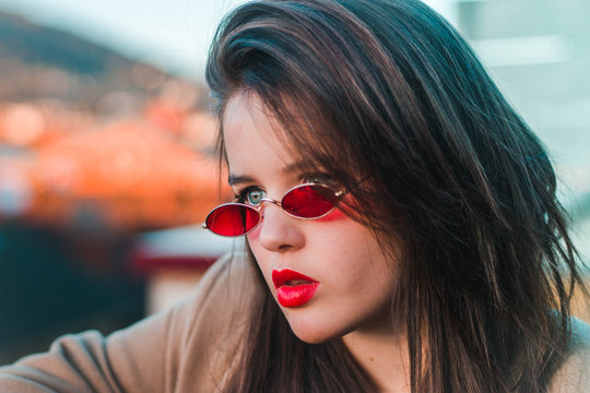 Girl with blue eyes and red lips wearing 80s glasses.