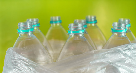 Bottlenecks of a pack of 8 empty and recyclable plastic water bottles, with no caps, sea green seal, inside a plastic bag, on a  colored vivid yellow background. garbage, Reuse, Eco-Friendly.