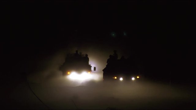 Military vehicles driving on dirt road at night